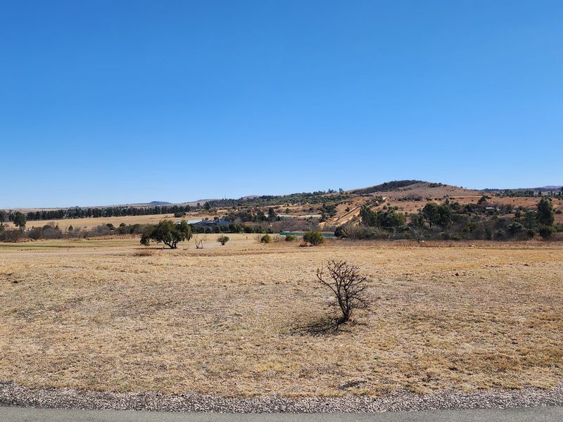 A wide-angle view of the expansive, undeveloped residential land featuring natural terrain and distant rolling hills under a clear blue sky.