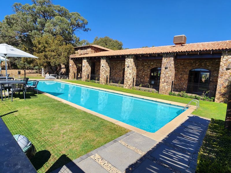 A well-maintained swimming pool area featuring a stone-clad building facade, terracotta roof tiles, and a spacious covered patio overlooking the pool.