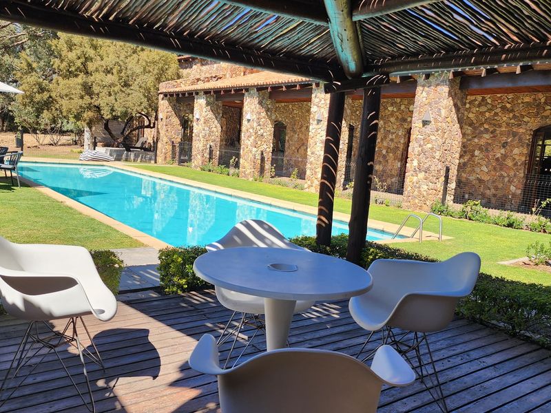 A well-maintained outdoor pool area featuring a swimming pool, stone-clad building facade, and a covered timber deck patio.