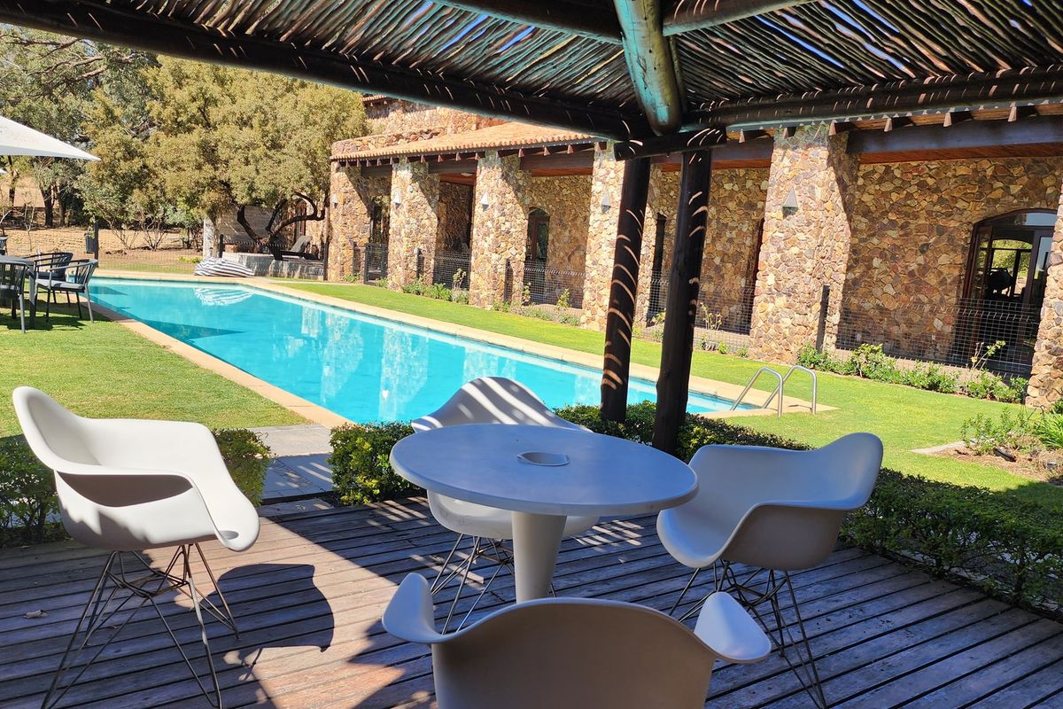 A well-maintained outdoor pool area featuring a swimming pool, stone-clad building facade, and a covered timber deck patio.