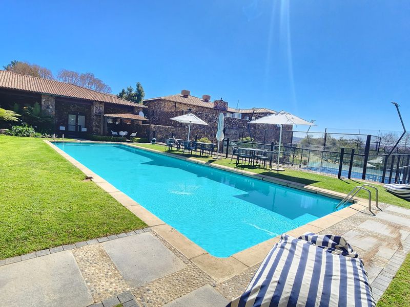 A well-maintained outdoor swimming pool area featuring stone-clad building exteriors, manicured lawn, and paved patio space, ideal for recreation and leisure.