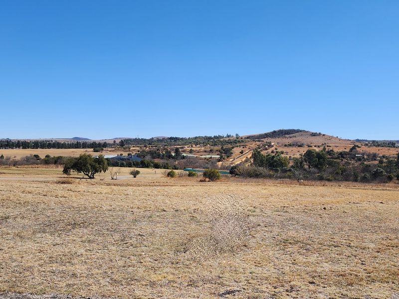 A wide-angle view of the expansive, undeveloped residential land featuring natural grass terrain and distant rolling hills under a clear blue sky.