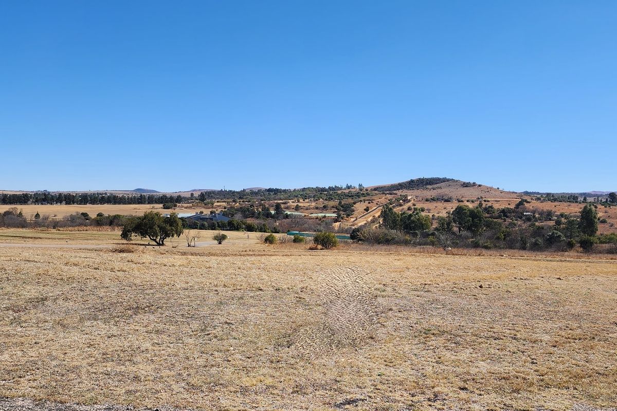 A wide-angle view of the expansive, undeveloped residential land featuring natural grass terrain and distant rolling hills under a clear blue sky.