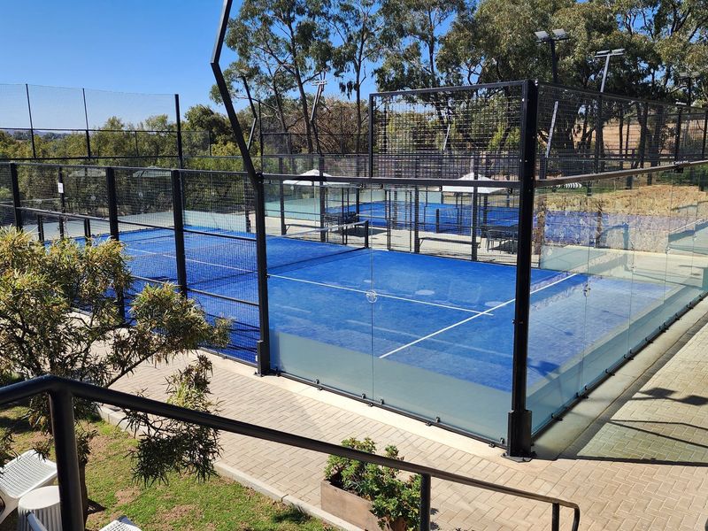 A well-maintained outdoor padel court featuring professional glass and mesh perimeter fencing, set within a landscaped recreational area.