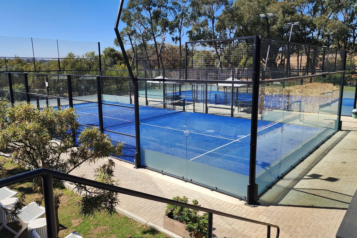 A well-maintained outdoor padel court featuring professional glass and mesh perimeter fencing, set within a landscaped recreational area.