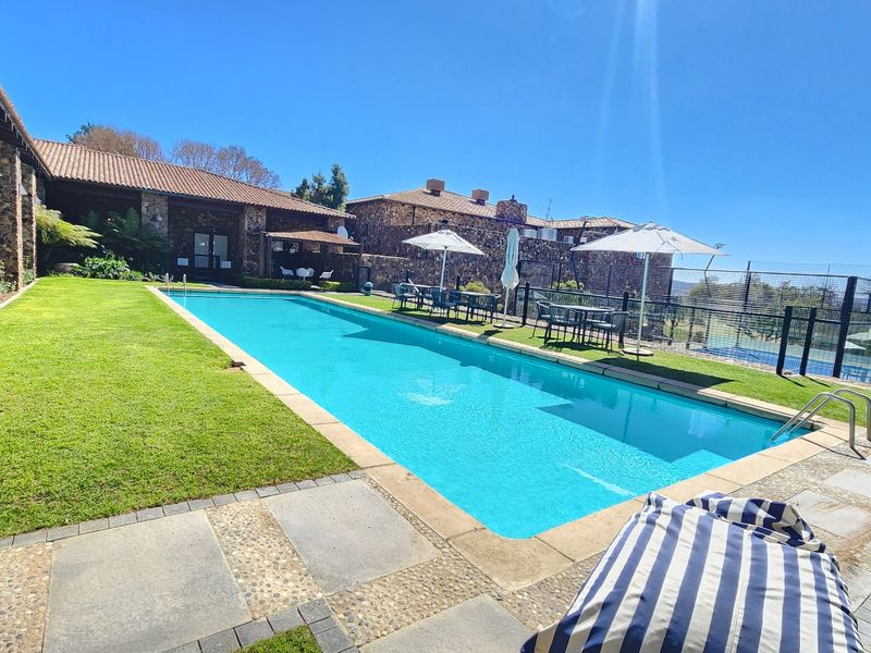 A well-maintained outdoor swimming pool area featuring stone-clad building exteriors, a manicured lawn, and paved patio space.