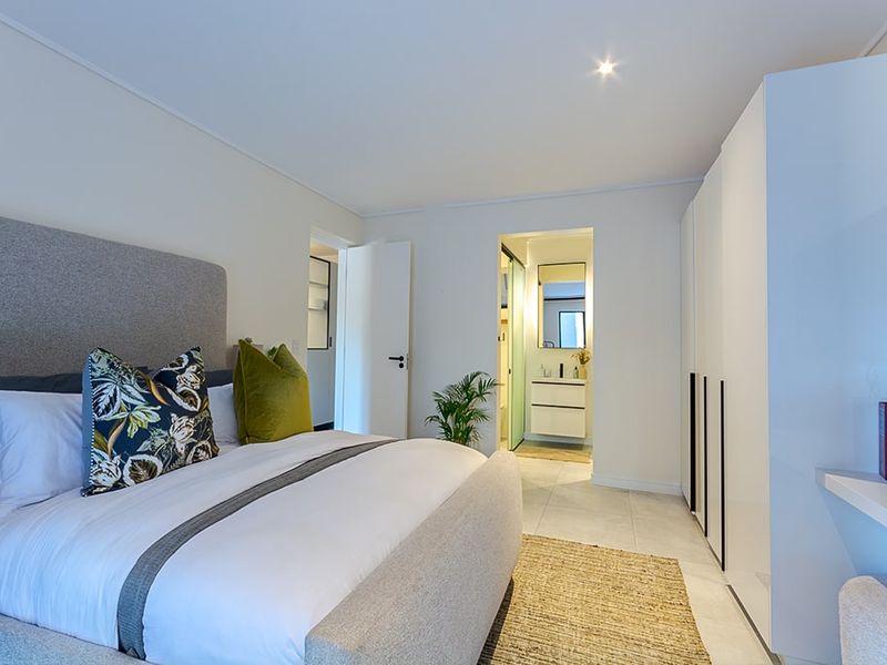 Modern bedroom featuring built-in cupboards, neutral tiled flooring, recessed lighting, and direct access to an en-suite bathroom.