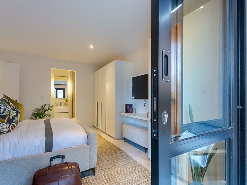 Modern bedroom featuring built-in cupboards, recessed lighting, and a sliding glass door leading to an outdoor area, with an adjoining en-suite bathroom.