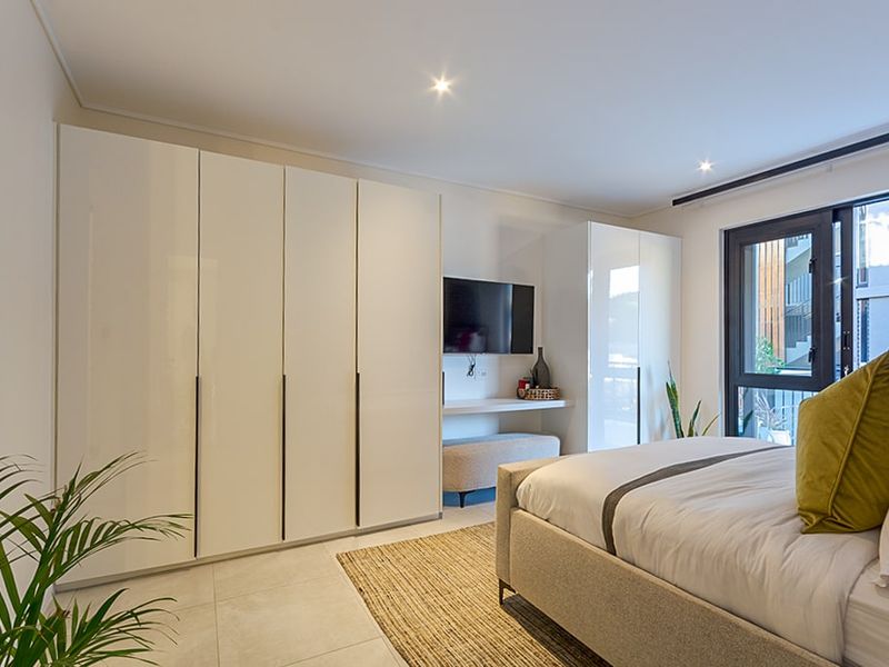 Modern bedroom featuring high-gloss built-in cupboards, tiled flooring, recessed downlighting, and direct access to an outdoor area through a sliding glass door.