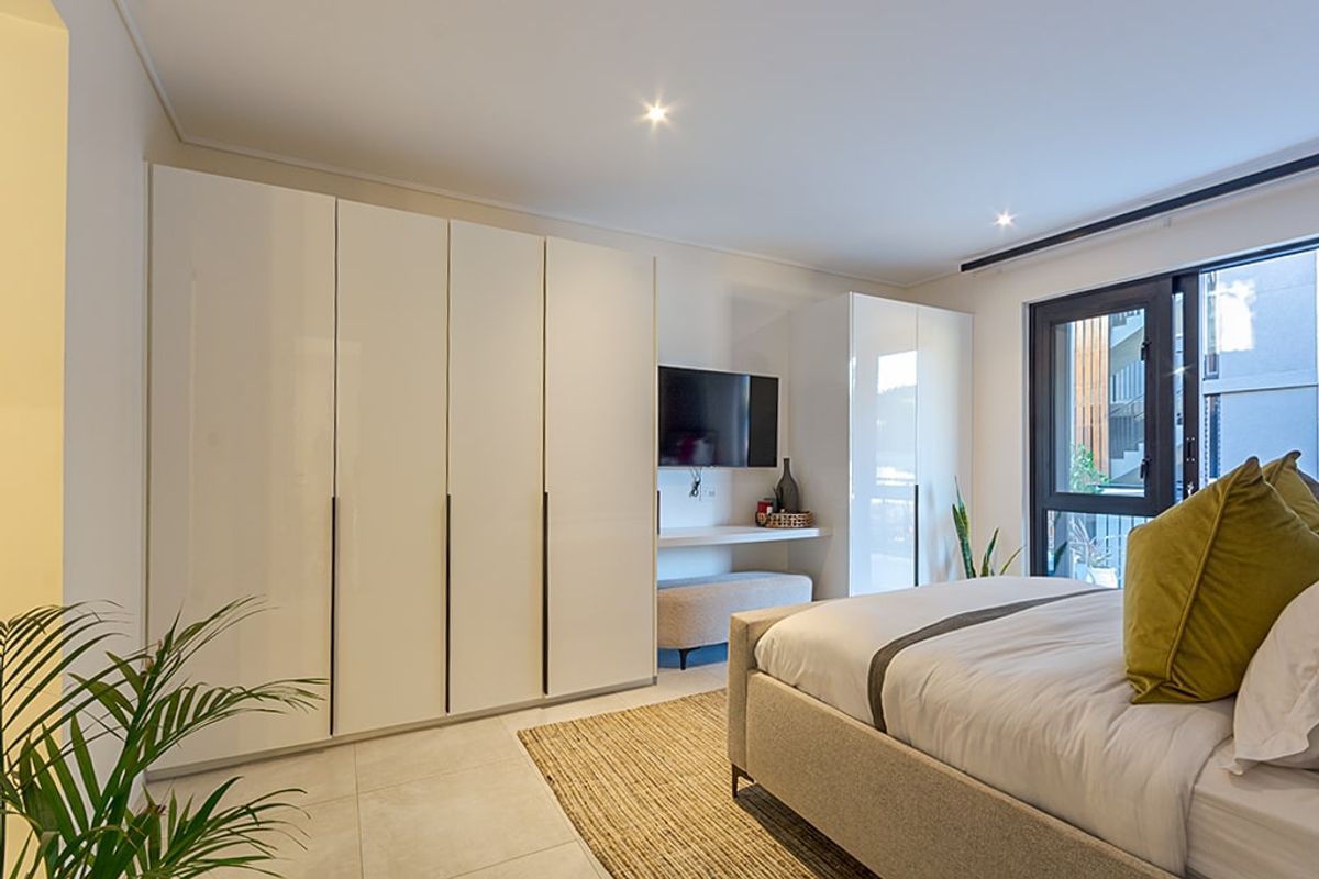 Modern bedroom featuring high-gloss built-in cupboards, tiled flooring, recessed downlighting, and direct access to an outdoor area through a sliding glass door.