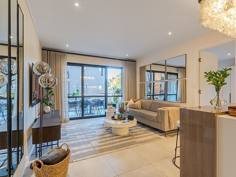 A bright and modern living room featuring tiled floors, recessed lighting, and large sliding glass doors that open onto a private balcony.