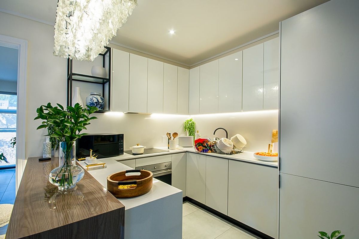 Modern kitchen featuring sleek white cabinetry, integrated appliances, stone countertops, and a functional breakfast bar with ambient under-cabinet lighting.