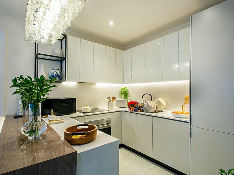 Modern kitchen featuring sleek white cabinetry, integrated appliances, stone countertops, and a functional breakfast bar with ambient under-cabinet lighting.
