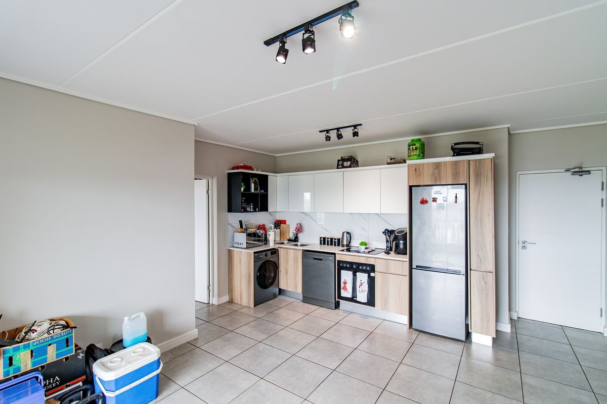 Modern kitchen featuring sleek white and wood-tone cabinetry, marble-look backsplash, tiled flooring, and integrated appliances with contemporary track lighting.