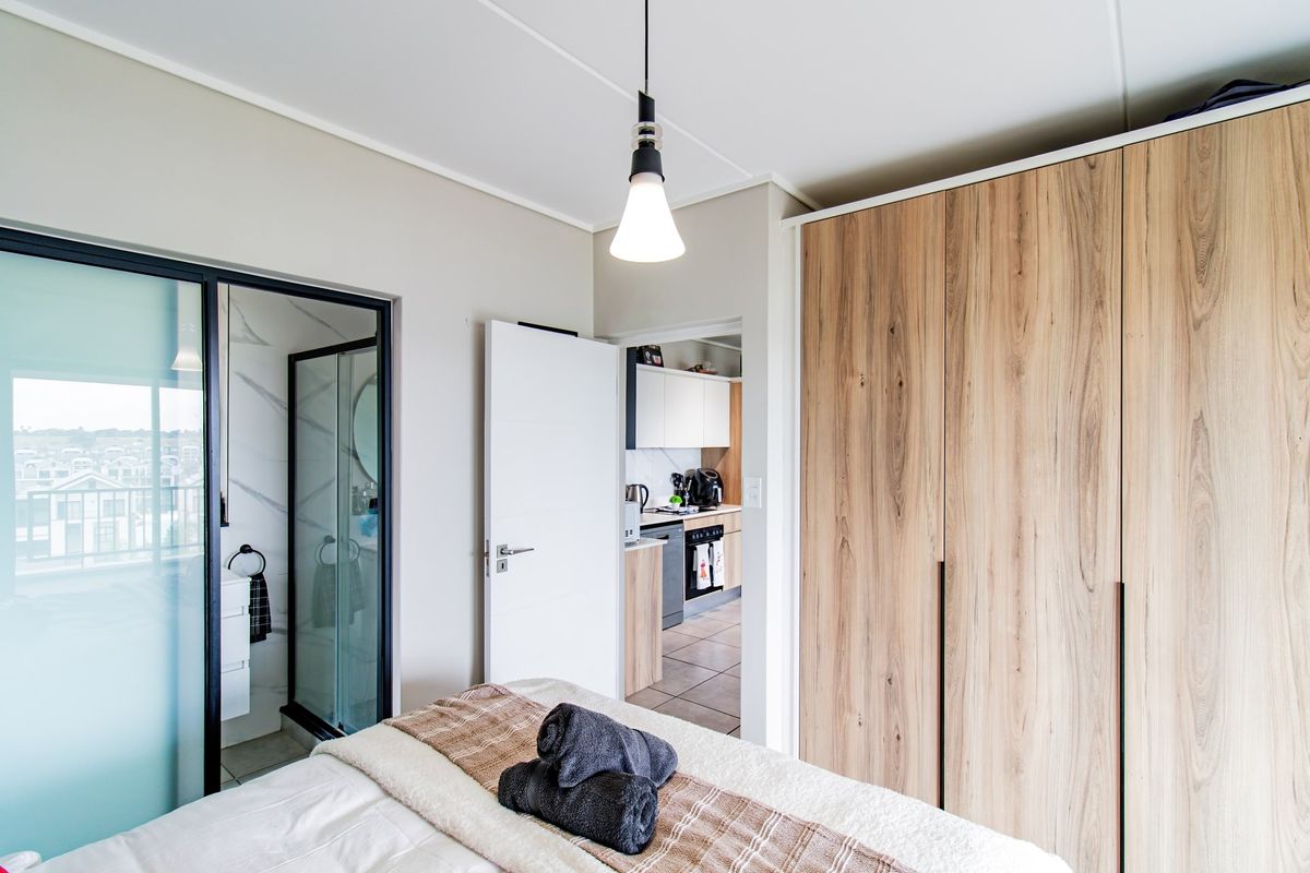 A modern bedroom featuring built-in wood-finish wardrobes, a pendant light, and direct access to an en-suite bathroom with a glass shower enclosure.