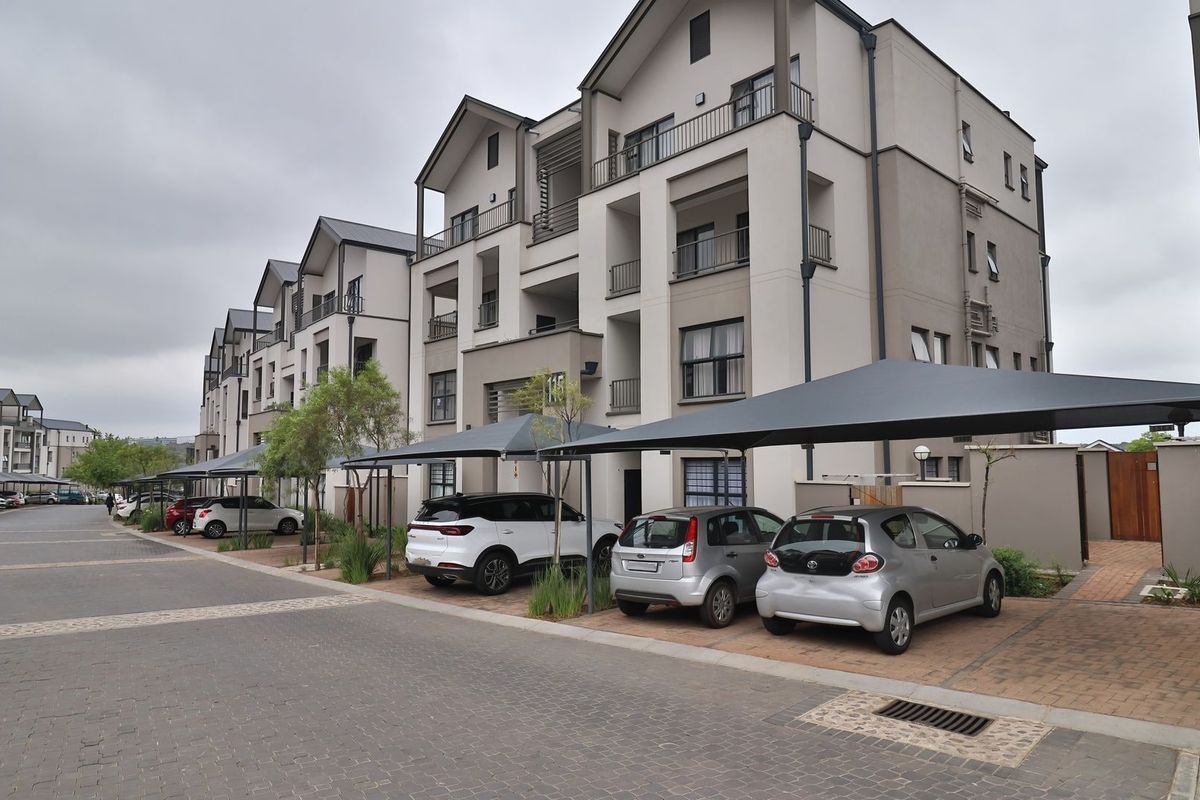 Exterior view of a modern multi-story apartment complex featuring paved parking areas with covered carports and balconies.