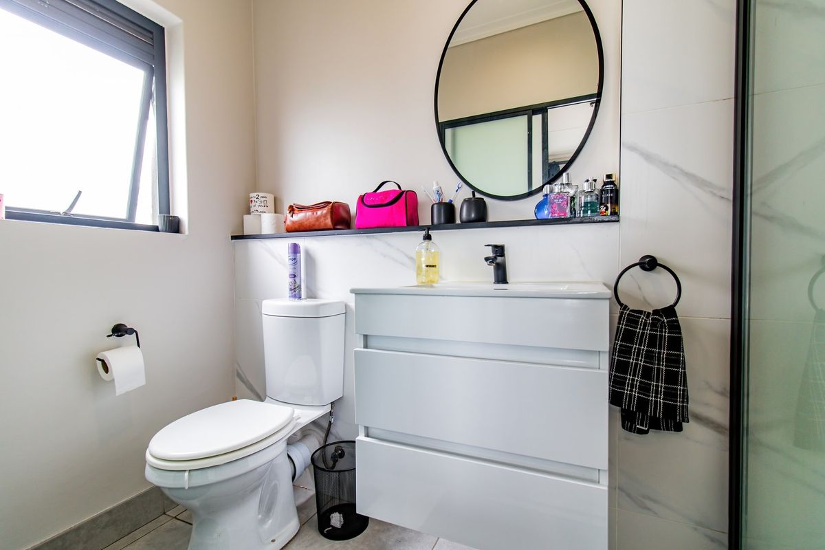 Modern bathroom featuring a sleek white vanity cabinet, basin, toilet, and marble-look wall tiles with a glass shower enclosure.