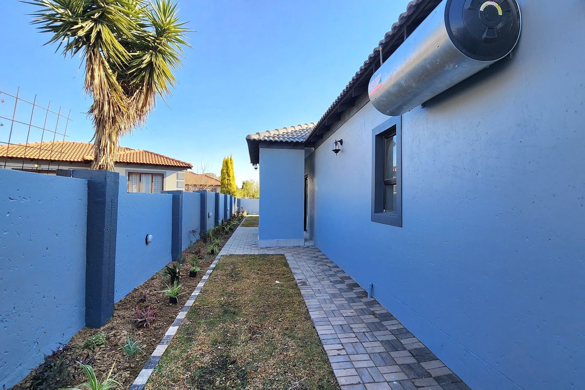 A well-maintained rear exterior area featuring a paved walkway, boundary wall, and an externally mounted solar geyser unit.