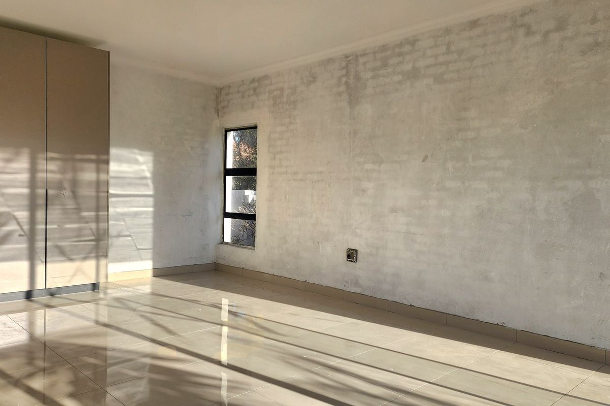 An empty bedroom featuring tiled flooring, a built-in wardrobe, and unfinished wall surfaces, offering a blank canvas for renovation and interior design.