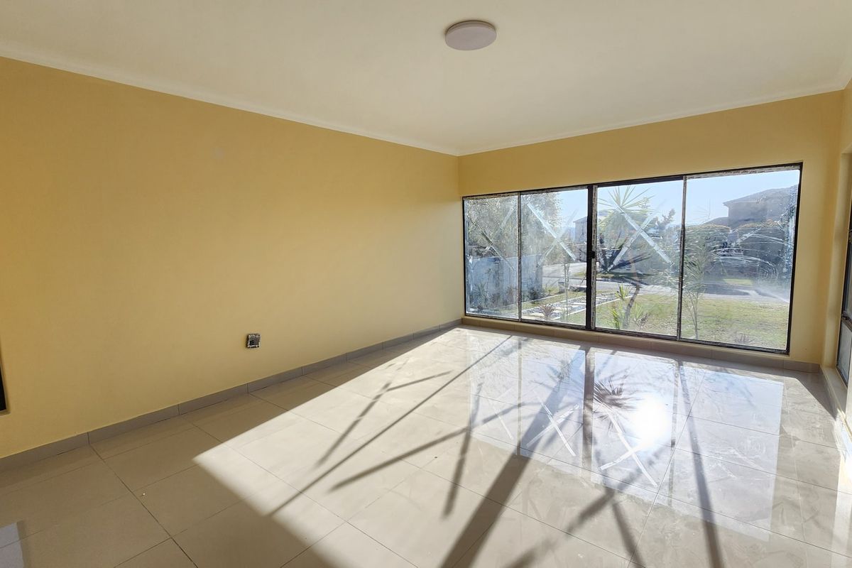 A bright, empty living room featuring large aluminium sliding windows and neutral tiled flooring, offering a clean canvas for interior design.