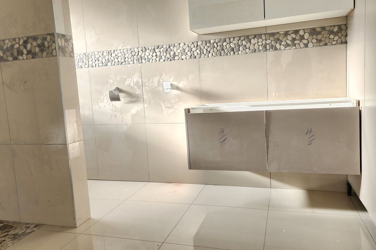 A bathroom in the final stages of construction, featuring tiled walls with a decorative pebble border and a wall-mounted vanity unit awaiting completion.