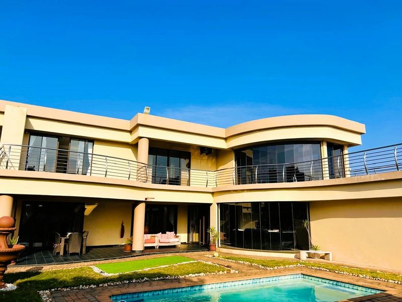 Rear view of a modern two-story residence featuring a swimming pool, covered patio, and an expansive upper-level balcony with glass sliding doors.