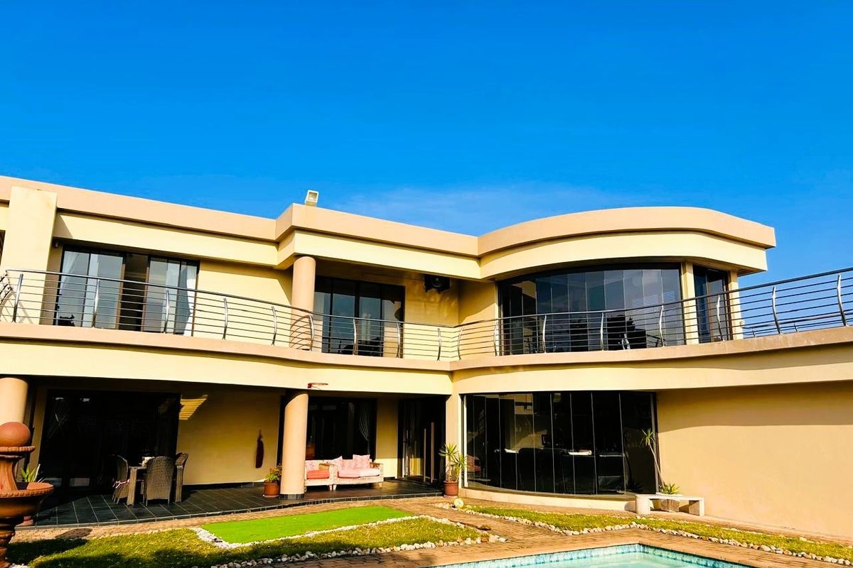 Rear view of a modern two-story residence featuring a swimming pool, covered patio, and an expansive upper-level balcony with glass sliding doors.