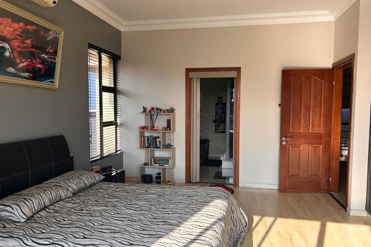 A well-maintained bedroom featuring laminate flooring, neutral wall tones, an air conditioning unit, and direct access to an en-suite bathroom.