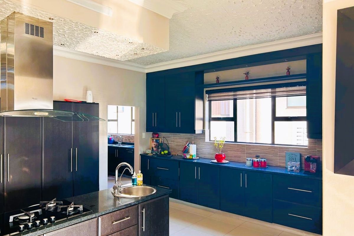 Modern kitchen featuring dark cabinetry, stone countertops, a gas hob, stainless steel extractor fan, and a secondary scullery area visible in the background.