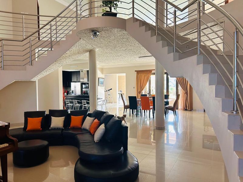 Spacious open-plan living and dining area featuring a grand central staircase with stainless steel balustrades and polished tile flooring.