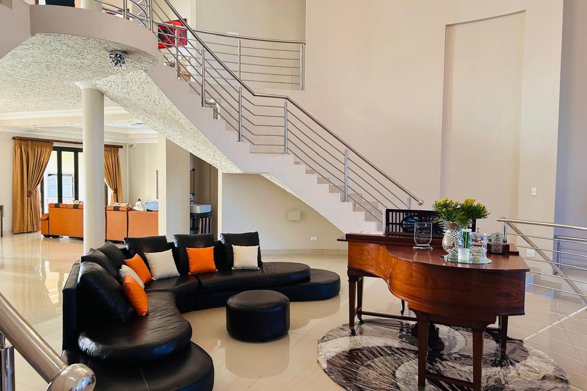 Spacious open-plan living area featuring a grand staircase with stainless steel railings, polished tile flooring, and high ceilings.