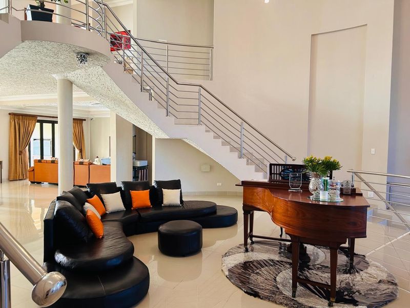 Spacious open-plan living area featuring a grand staircase with stainless steel railings, polished tile flooring, and high ceilings.