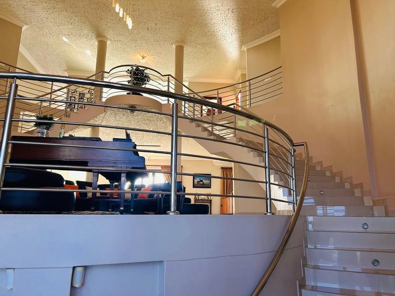 Grand entrance hall featuring a striking curved staircase with a modern stainless steel balustrade and elegant tiled flooring.