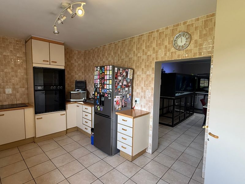 A functional kitchen featuring built-in oven, hob, and tiled splashbacks, with an open-plan layout leading into an adjacent living area.