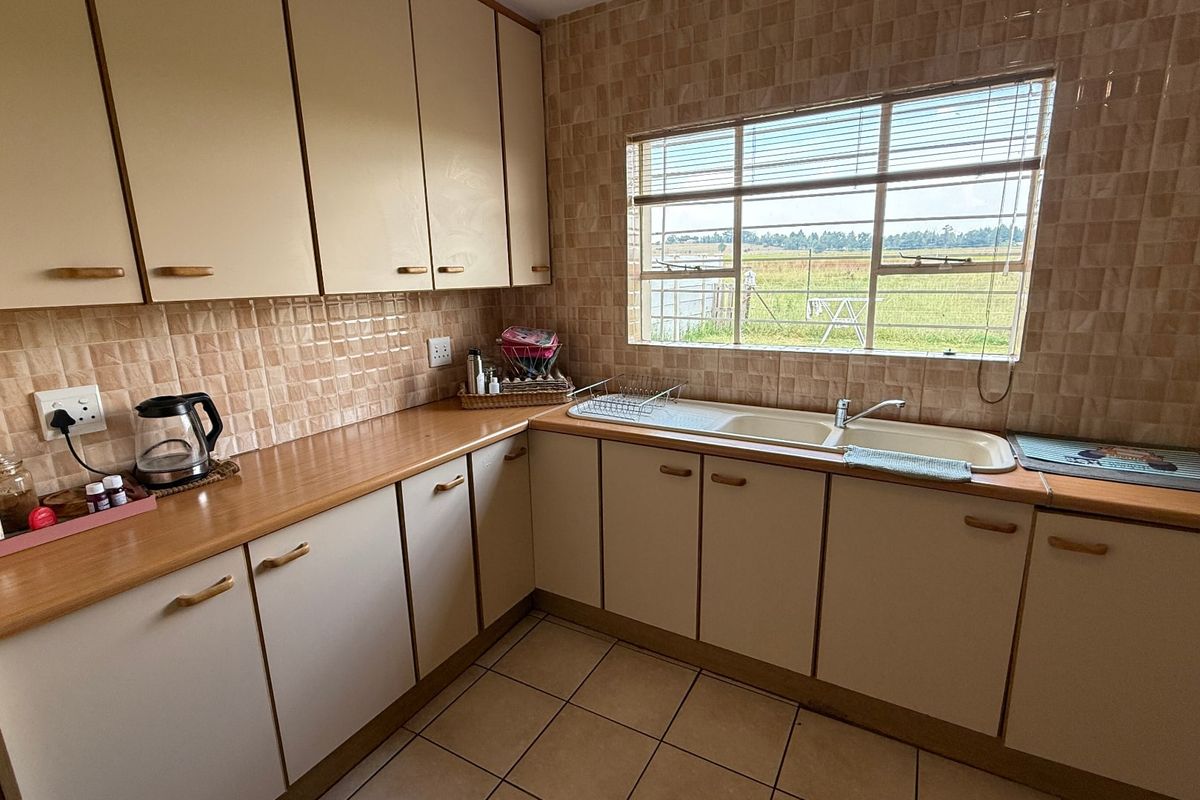 A functional kitchen featuring laminate countertops, built-in cabinetry, a double basin sink, and tiled flooring with a view of the surrounding landscape.
