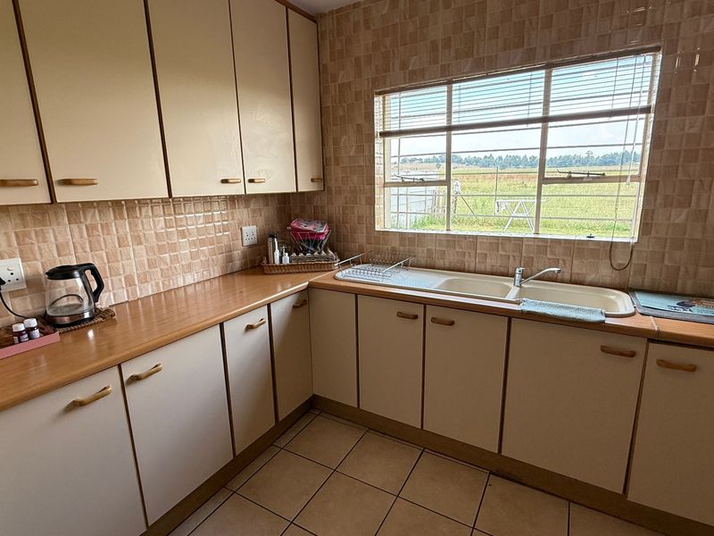 A functional kitchen featuring laminate countertops, built-in cabinetry, a double basin sink, and tiled flooring with a view of the surrounding landscape.