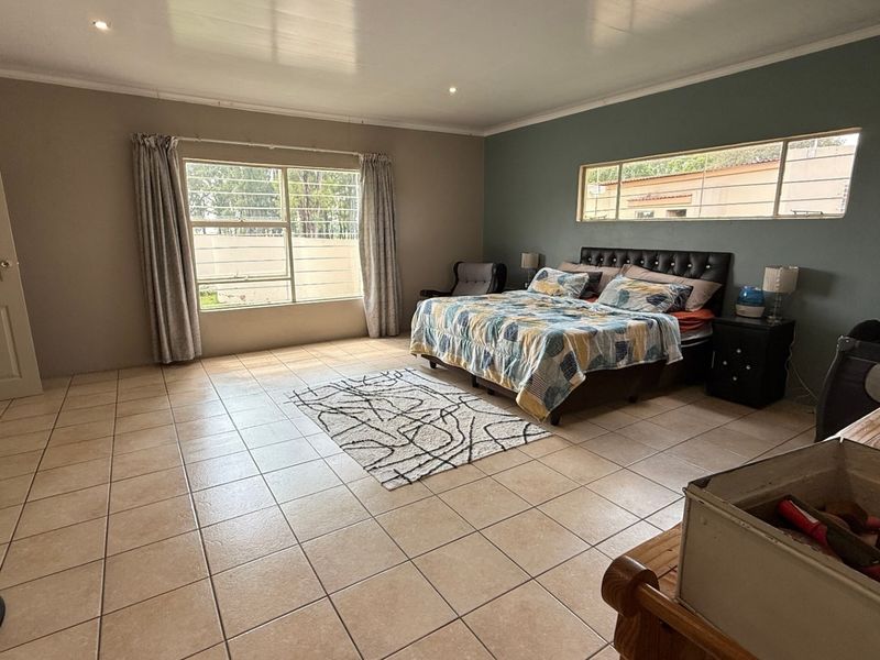 Spacious bedroom featuring large windows with security bars, tiled flooring, and a neutral color palette.