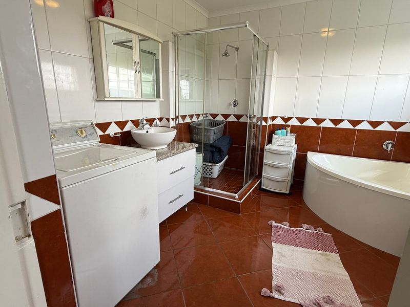 A functional bathroom featuring a corner bathtub, separate glass-enclosed shower, vanity basin, and integrated laundry space with tiled flooring and wall finishes.
