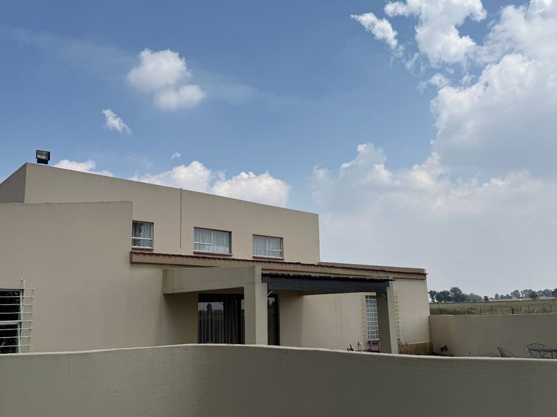 Rear view of a two-story residential property featuring a covered patio area, perimeter boundary walls, and expansive rural landscape views.