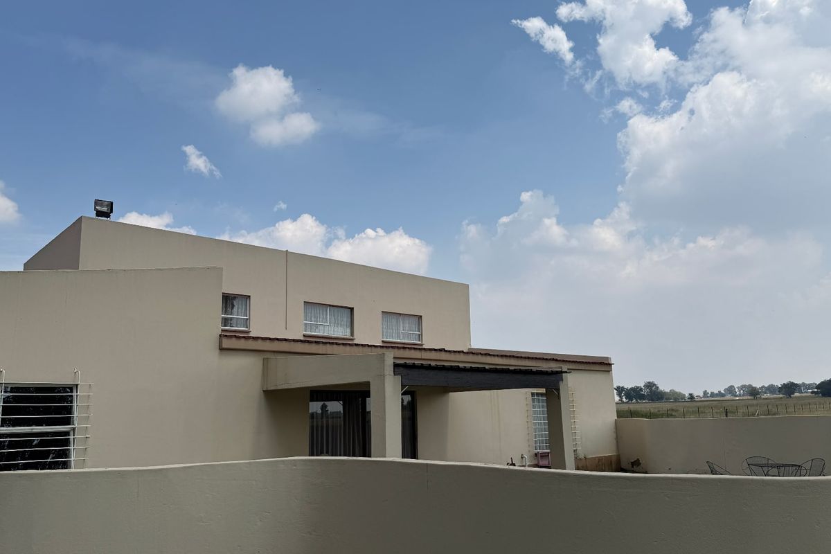 Rear view of a two-story residential property featuring a covered patio area, perimeter boundary walls, and expansive rural landscape views.