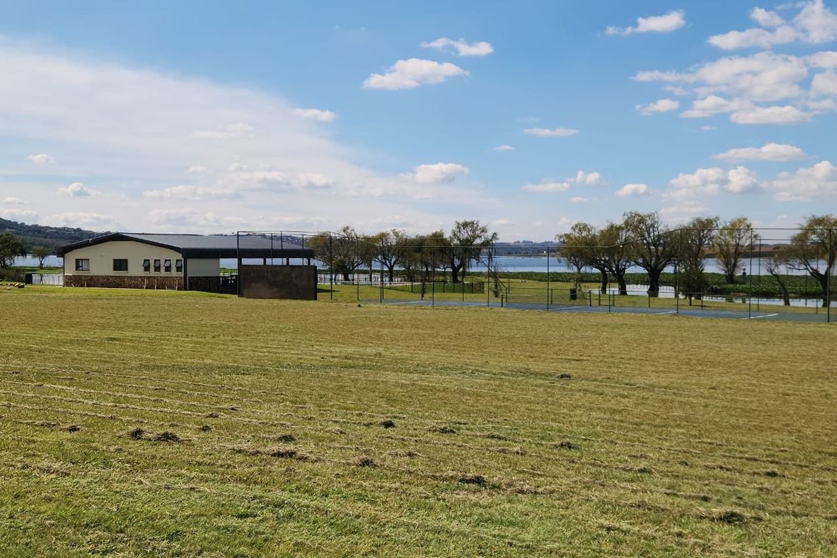 Expansive residential land featuring a sports facility, stone-clad building, and scenic water views in a peaceful, open setting.