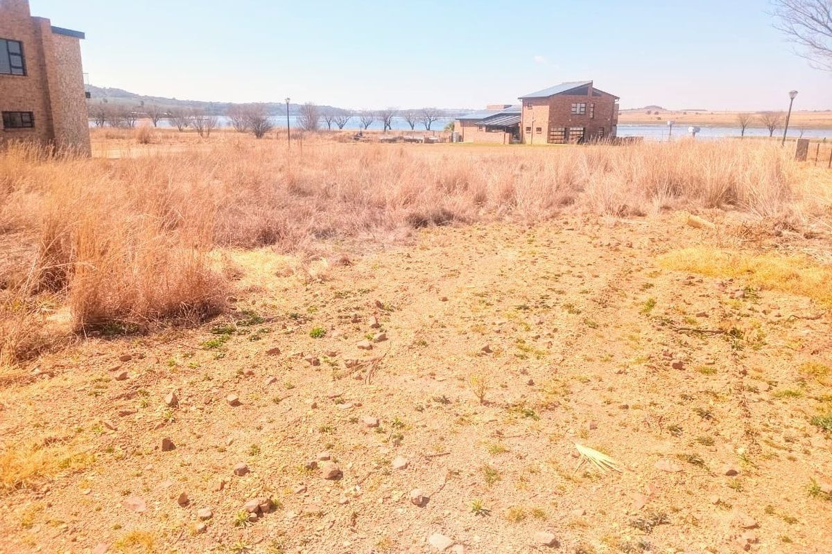 A view of a vacant residential plot featuring natural dry vegetation and soil, with neighboring properties visible in the background.