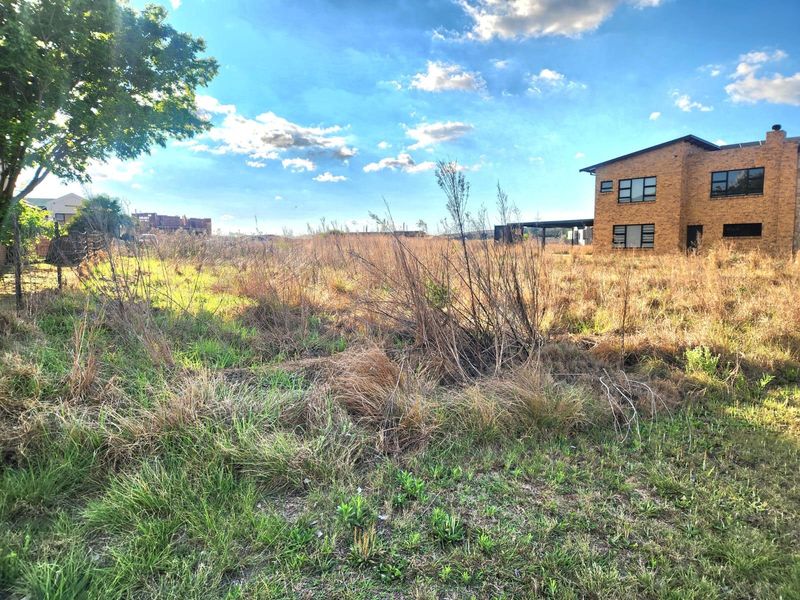 A vacant residential plot featuring overgrown grass and natural vegetation, situated in a developed neighborhood setting.