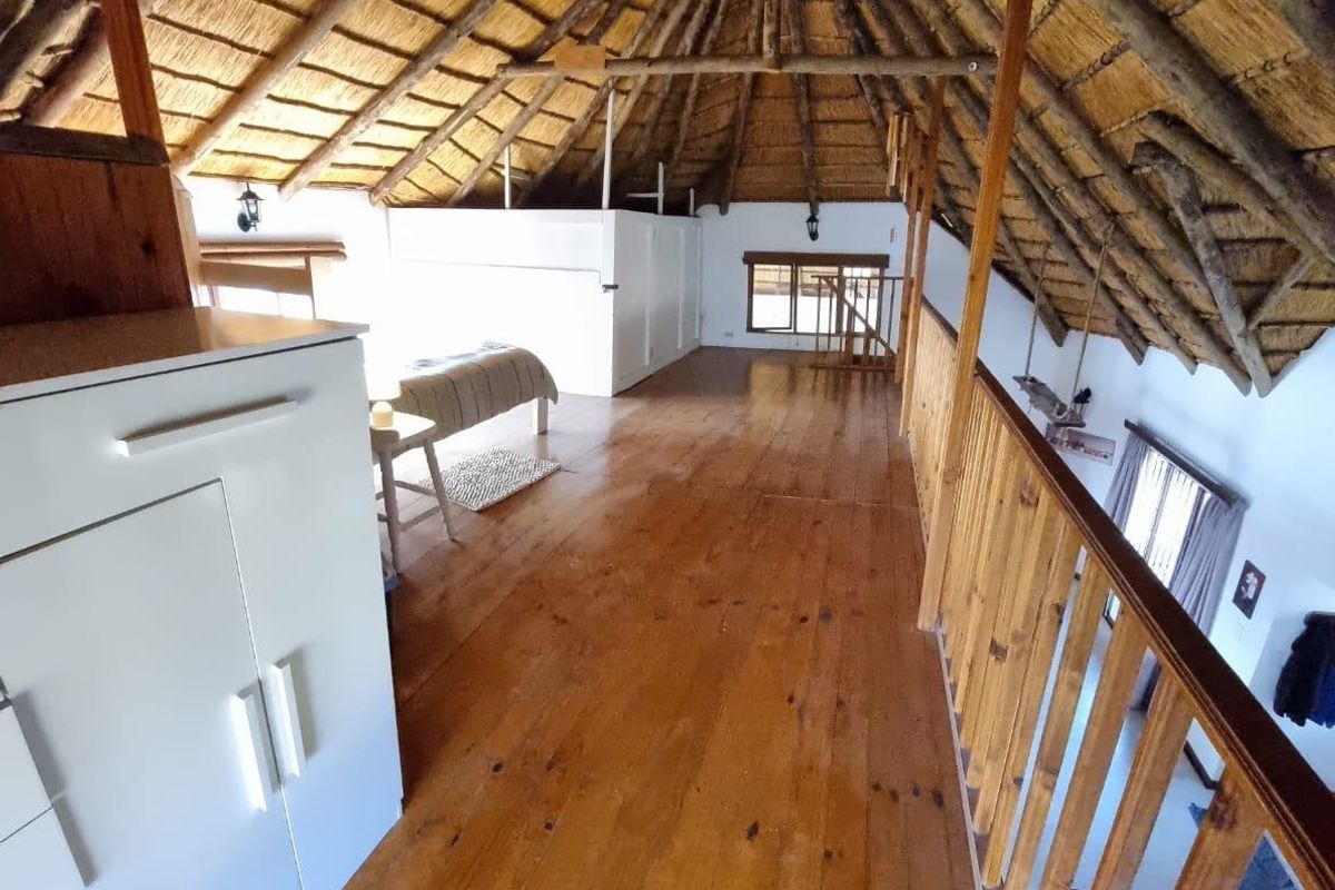 Spacious loft bedroom featuring a traditional thatched roof with exposed timber rafters, polished wooden flooring, and a timber balustrade overlooking the lower level.