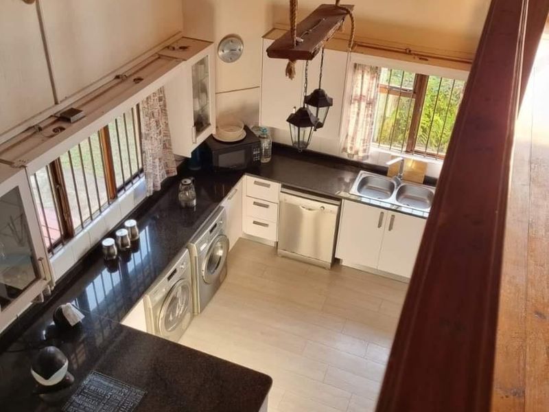 A functional kitchen featuring granite countertops, built-in cabinetry, integrated appliances, and tiled flooring, viewed from an elevated mezzanine level.