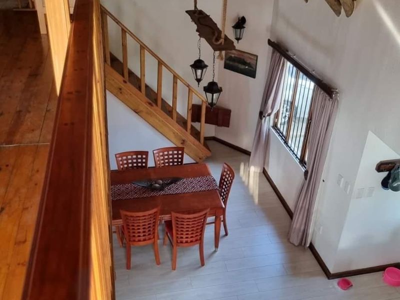 Dining area featuring a wooden staircase, exposed timber ceiling beams, and tiled flooring, viewed from an elevated mezzanine level.