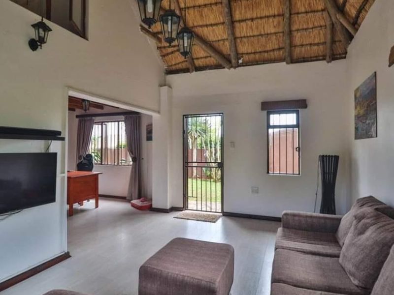 Spacious living area featuring a high thatched ceiling with exposed timber rafters, laminate flooring, and direct access to the garden through a security gate.