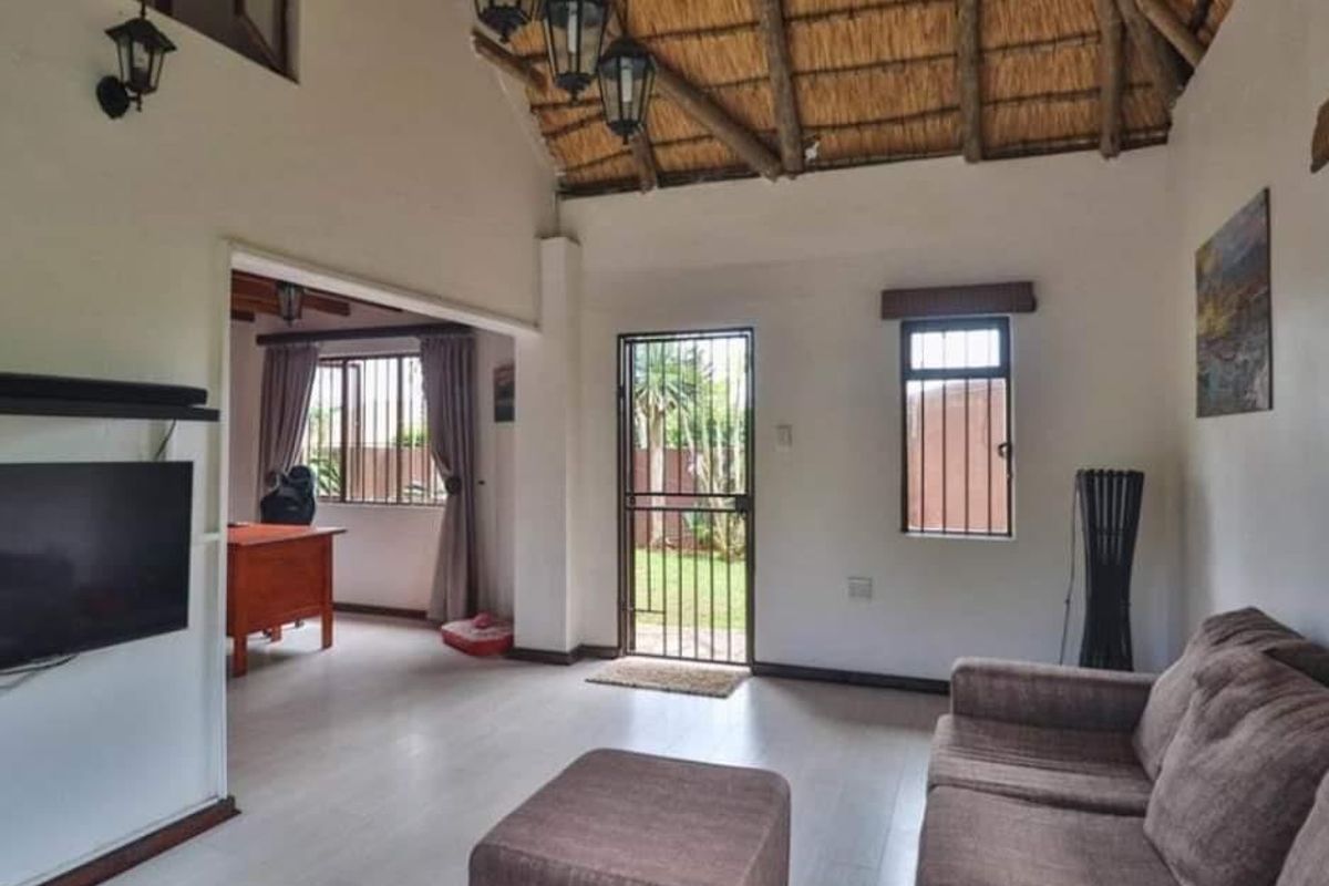 Spacious living area featuring a high thatched ceiling with exposed timber rafters, laminate flooring, and direct access to the garden through a security gate.
