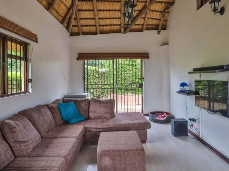 A living room featuring a high vaulted thatched ceiling with exposed timber rafters, laminate flooring, and sliding glass doors leading to the exterior.