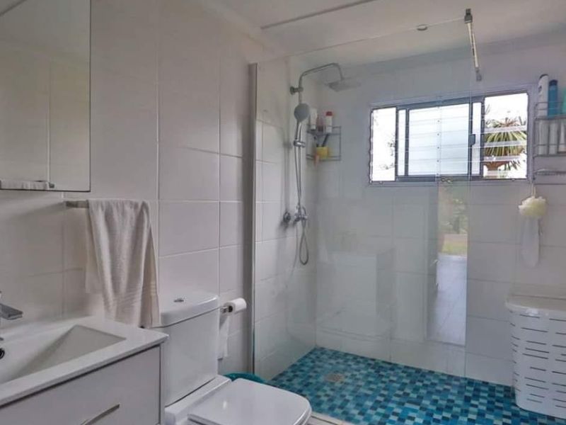 A clean, functional bathroom featuring a vanity cabinet, a glass-enclosed shower with mosaic floor tiling, and a louver window for natural ventilation.